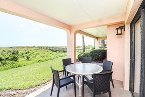 A covered outdoor seating area with a table and chairs, overlooking a grassy landscape and a wooden bridge. - Sea Place 11110-Three Bedroom Condo in Popular Sea Place Community (St. Augustine)