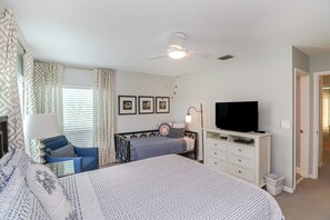 Ein Schlafzimmer mit Bett, Schreibtisch, Fernseher und Deckenventilator.