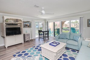 A living room with a TV, sofa, coffee table, and a balcony with chairs.