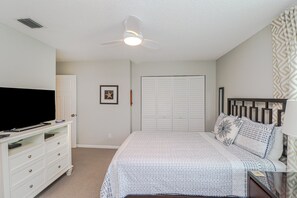 A bedroom with a bed, a dresser, a television, a ceiling fan, and a closet.