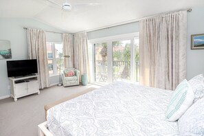 Ein Schlafzimmer mit einem Bett, einem Fernseher, einem Sessel und einem Balkon mit Vorhängen.