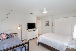 A bedroom with two beds, a dresser, a television, and a ceiling fan.