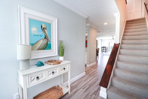 A hallway with a white console table, a framed artwork, a lamp, and a staircase.