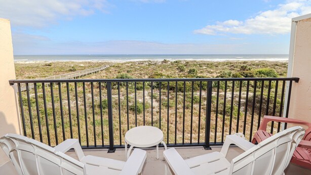 Un balcon avec vue sur la plage, des chaises blanches et une petite table.