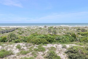 Un paysage côtier avec une promenade en bois menant à la plage, le tout entouré d’une végétation luxuriante.