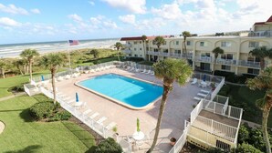 Een hotel met een zwembad, palmbomen en uitzicht op het strand.