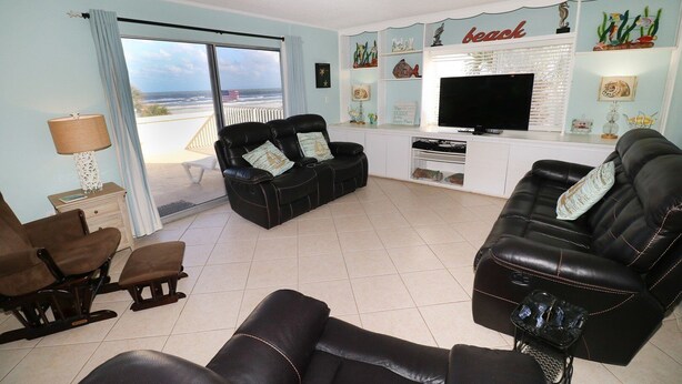 Een woonkamer met een bank, stoelen, een televisie en uitzicht op de oceaan.