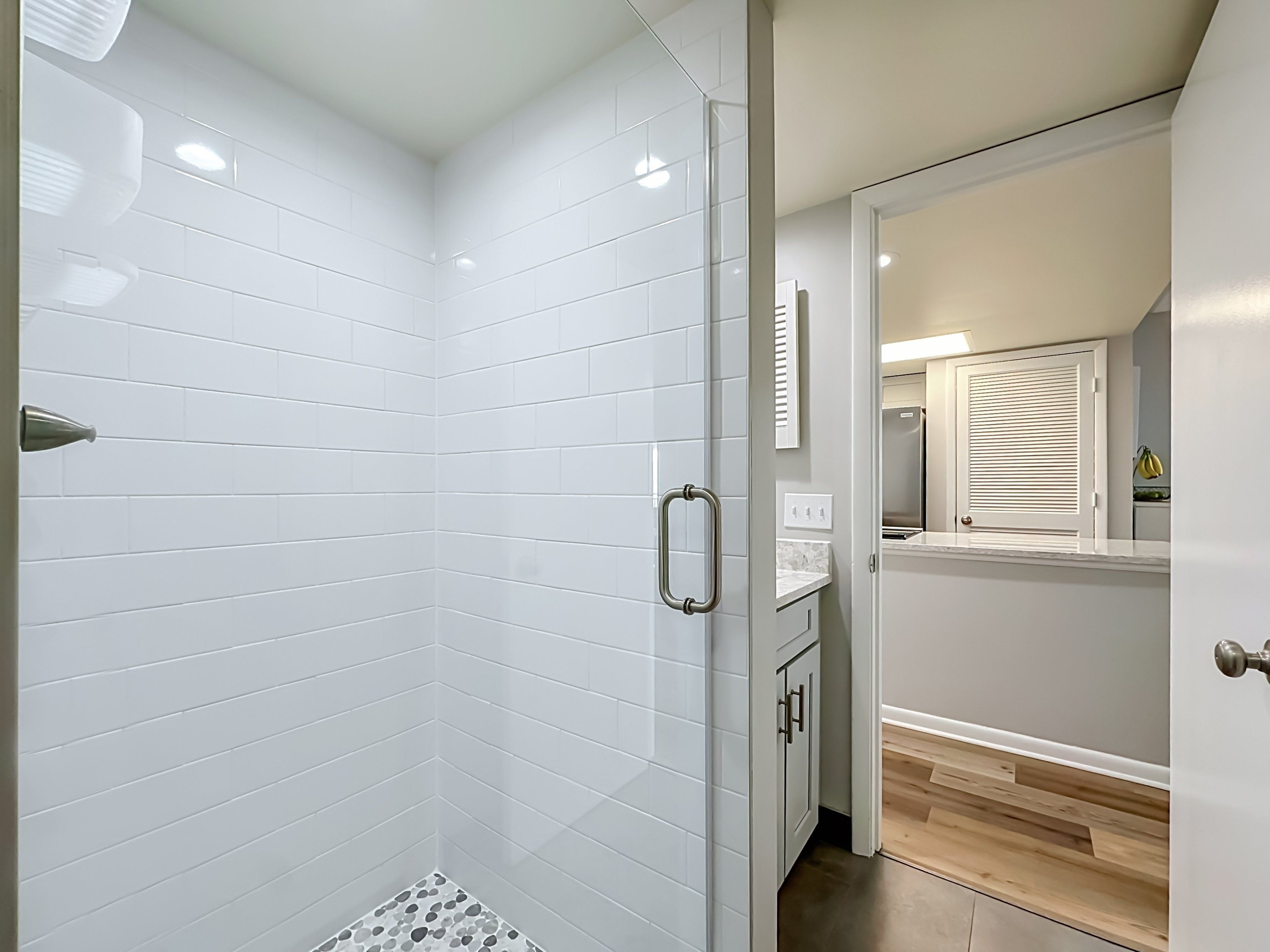 A modern bathroom with white subway tiles, a shower with a glass door, and a wooden floor.