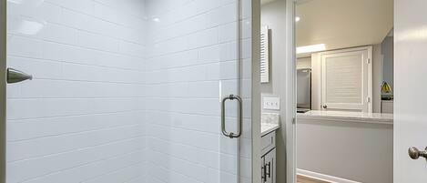 A modern bathroom with white subway tiles, a shower with a glass door, and a wooden floor.