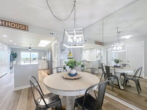 A modern kitchen with a central island, a dining area with a round table and chairs, and a view of the outside.