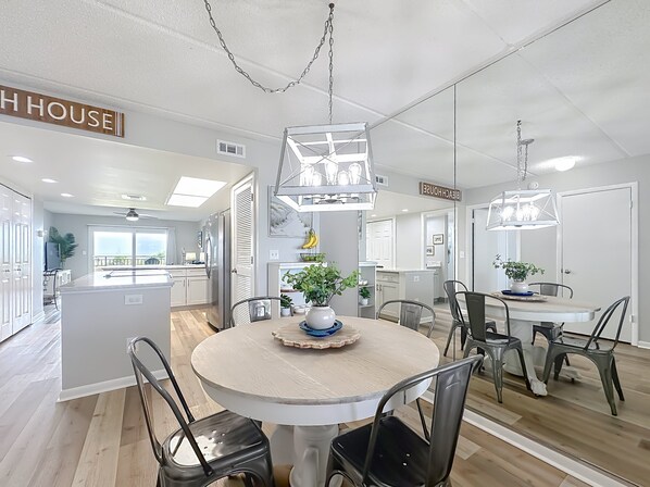 A modern kitchen with a central island, a dining area with a round table and chairs, and a view of the outside.