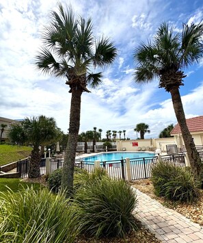 A swimming pool surrounded by palm trees and a brick pathway.