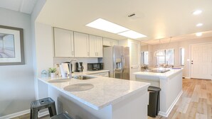 Une cuisine moderne avec des meubles blancs, un îlot central doté d’un évier et un réfrigérateur.