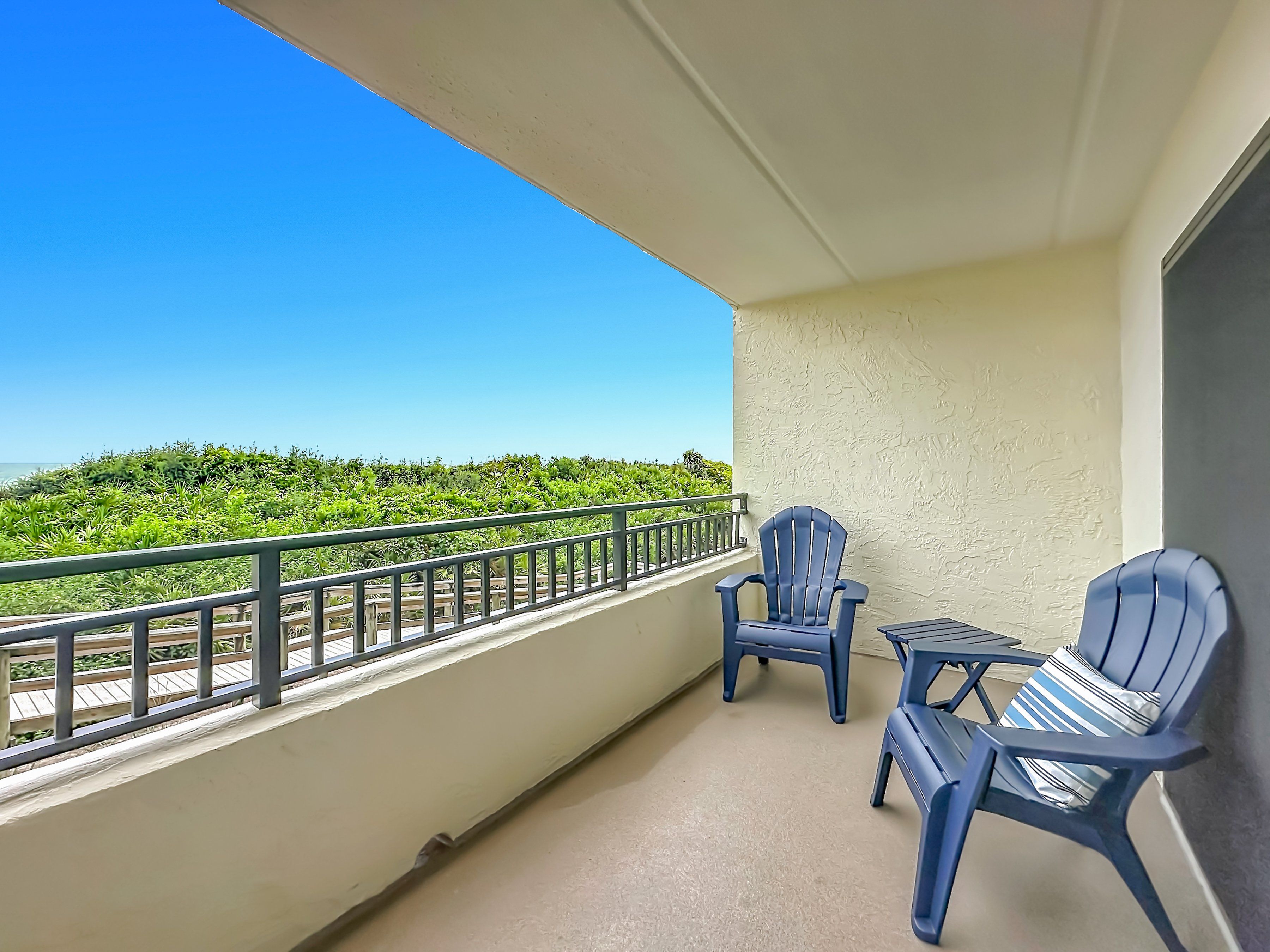Un balcon avec deux chaises et une petite table, offrant une vue sur un paysage verdoyant et luxuriant ainsi que sur la mer.