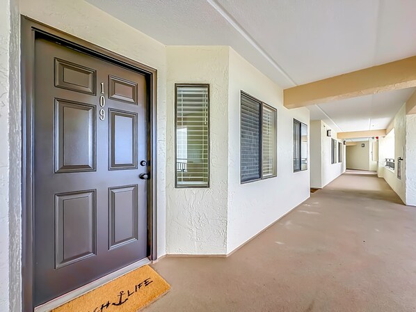 Un pasillo con una puerta marrón oscuro, paredes color beige y una felpudo con la palabra 'WELCOME'.