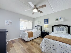Ein Schlafzimmer mit zwei Betten, einem Deckenventilator, einem Fenster mit Jalousien und einer Wand mit einem dekorativen Schild.