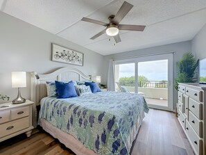 Ein Schlafzimmer mit einem Bett, Nachttischen, einem Deckenventilator, einem großen Fenster und Blick ins Freie.