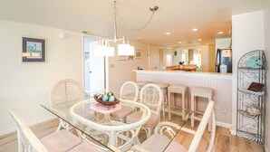 A dining area with a glass table, wicker chairs, and a chandelier. - Windjammer 212 - Direct Oceanfront, Intracoastal Waterway Views in Crescent Beach (St. Augustine)