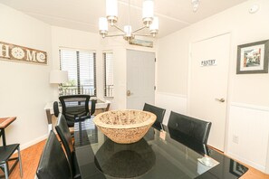 A dining area with a glass table, black chairs, a woven centerpiece, and a chandelier.