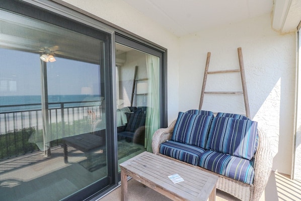 A balcony with a wicker sofa and a wooden table, a sliding glass door, and a ladder leaning against the wall.