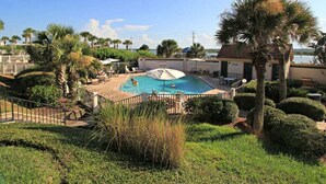 A swimming pool with a view of the water, surrounded by palm trees and a building. - Windjammer 312 - Remodeled, Direct Oceanfront Three Bedroom Crescent Beach Condo (St. Augustine)