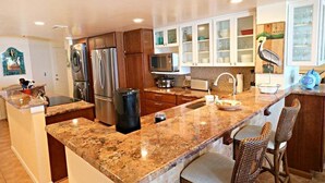 A modern kitchen with granite countertops, stainless steel appliances, and a central island with bar stools. - Windjammer 312 - Remodeled, Direct Oceanfront Three Bedroom Crescent Beach Condo (St. Augustine)