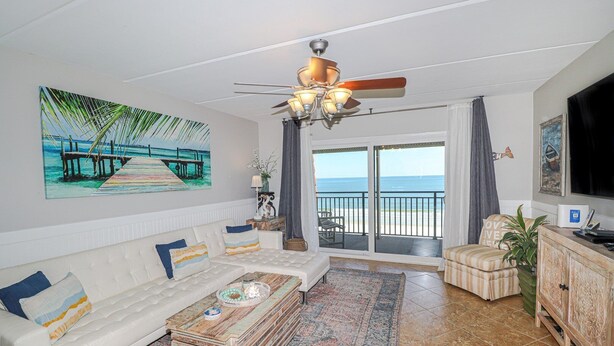A living room with a white sofa, a coffee table, a TV, and a view of the beach through a sliding door. - Windjammer 404 - Updated, 4th Floor Oceanfront Condo with Elevator Access (St. Augustine)