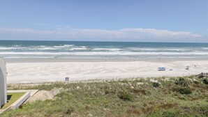 A beach with a clear view of the ocean, a sandy shore, and a grassy area with a structure in the foreground.