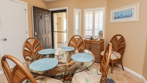 A dining area with a glass table surrounded by wicker chairs, a cabinet with decorative items, and a door with a number sign.