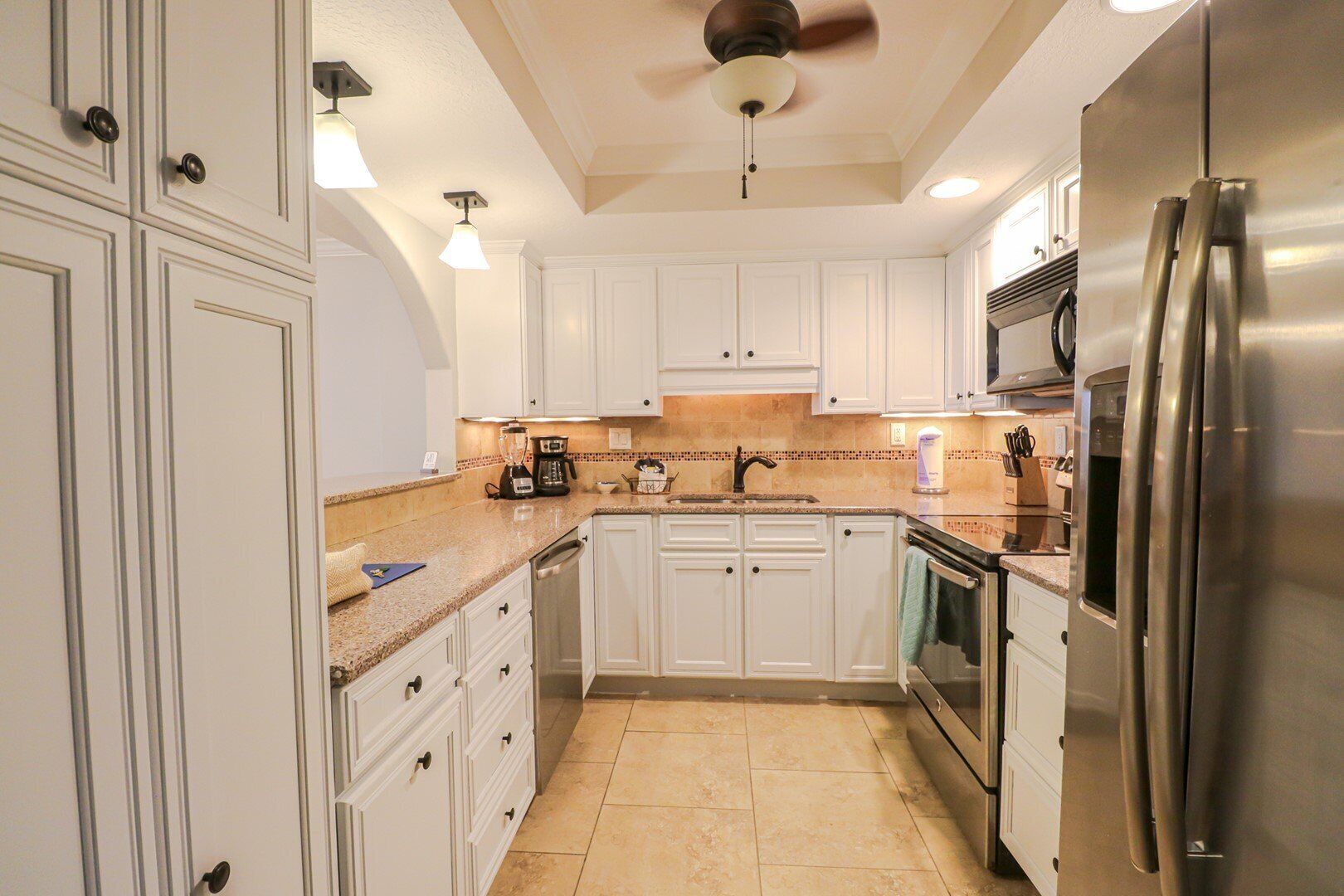 A kitchen with white cabinets, a stainless steel refrigerator, a coffee maker, and a ceiling fan.