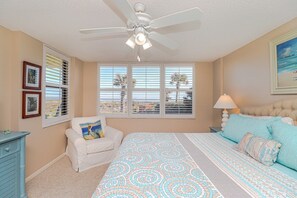 A bedroom with a bed, a chair, a desk, a ceiling fan, and a window with blinds. - Barefoot Trace 105-Direct Oceanfront Views from Private Balcony, Pet Friendly (St. Augustine)