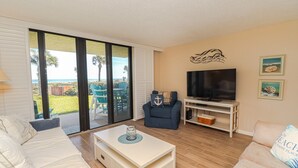 Una sala de estar con televisor, sofá, mesa de centro y vista al exterior.