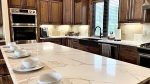 A kitchen with a long island, dark wooden cabinets, stainless steel appliances, and a window with blinds. - Luxury Mountain Home in Grand Lake - Hot Tub (Grand Lake)