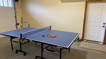 A ping pong table in a room with a door, a window, and a wall-mounted electrical outlet.