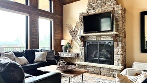 A cozy living room with a stone fireplace, leather sofa, and large windows. - Luxury Mountain Home in Grand Lake - Hot Tub (Grand Lake)