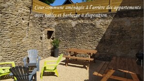 A courtyard with stone walls, a wooden table, and chairs. - Porte Vannetaise - Studio - 20m² - Maximum 2 Personnes (Guérande)