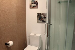 A bathroom with a toilet, a glass shower enclosure, and two framed pictures on the wall. - Porte Vannetaise - Studio - 20m² - Maximum 2 Personnes (Guérande)