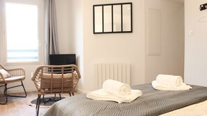 A bedroom with a bed, two rolled towels, a chair, a television, and a window with curtains. - Porte Vannetaise - Studio - 20m² - Maximum 2 Personnes (Guérande)