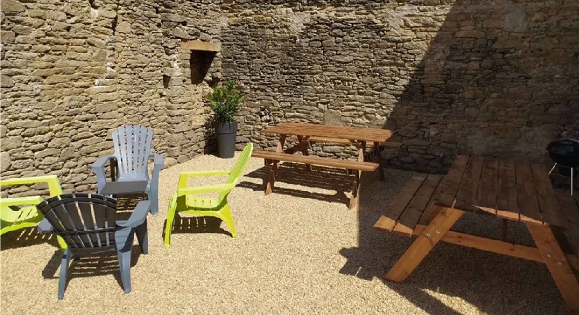 Une cour avec des murs en pierre, une table en bois et des chaises.