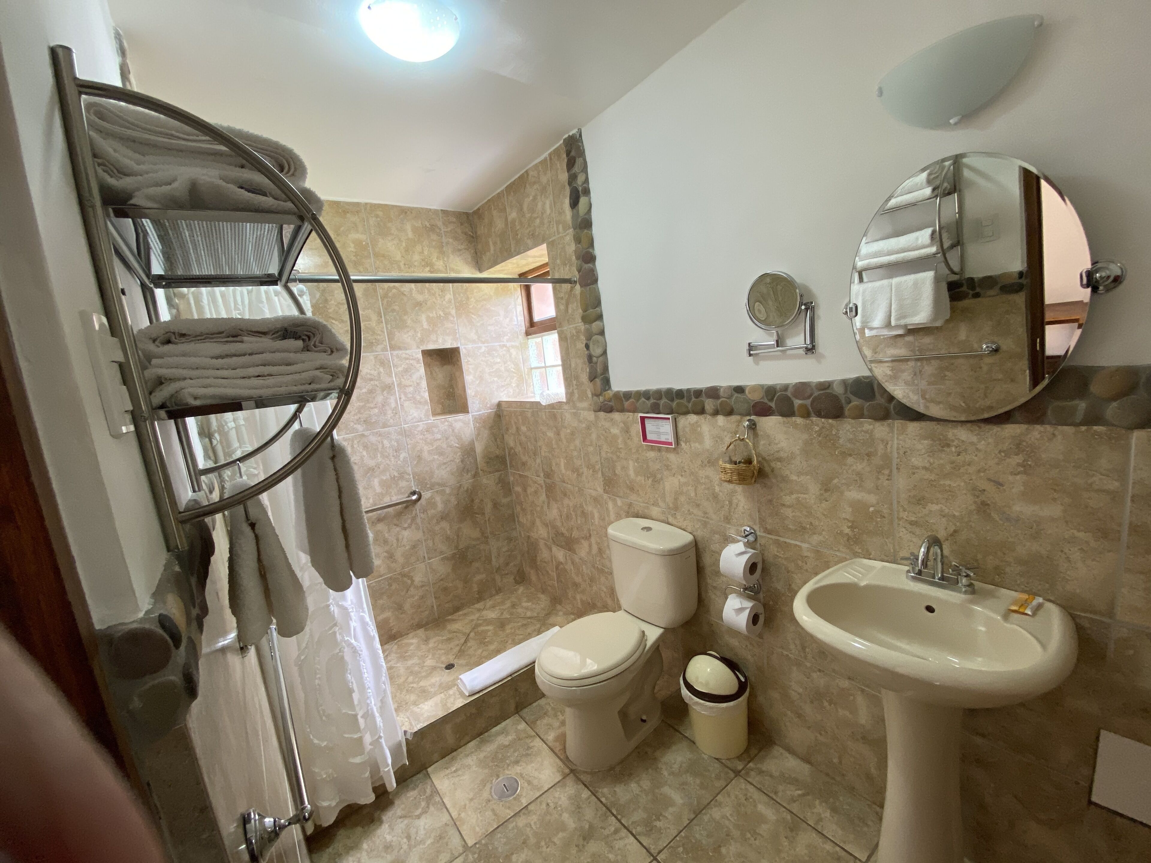 A bathroom with a shower, toilet, sink, and a towel rack with folded towels.