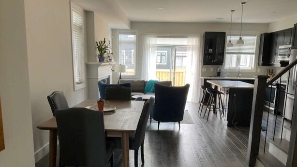 Eine moderne Küche mit dunklen Schränken, ein Essbereich mit Holztisch und -stühlen sowie ein Blick ins Freie durch große Fenster.