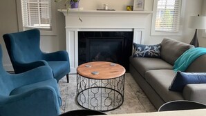 Ein Wohnzimmer mit Kamin, blauen Sesseln, einem runden Couchtisch und einem Sofa mit blauer Decke.