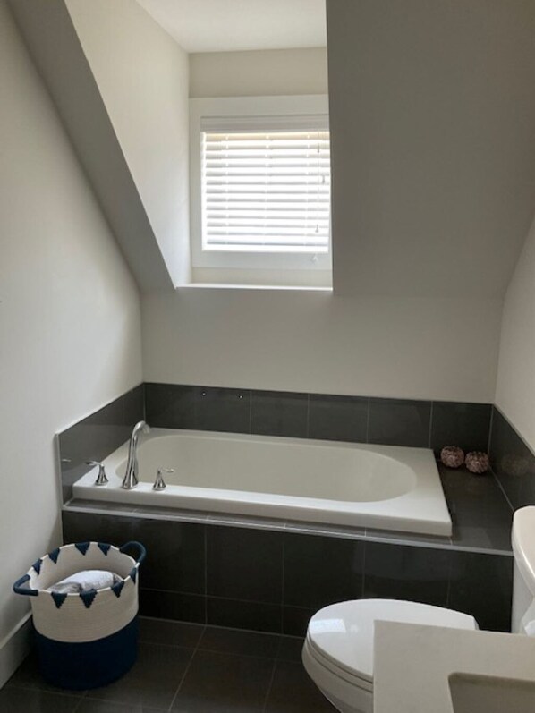 Une salle de bain avec une baignoire, des toilettes et une fenêtre avec des stores.