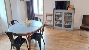 Ein Essbereich mit einem runden Tisch, Stühlen, einem Schrank mit Glastüren, einem Fernseher und einem Fenster mit Vorhängen.