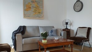 Ein Wohnzimmer mit einer Couch, einem Couchtisch mit Pflanze und Gläsern, einer Wanduhr und einer Karte.