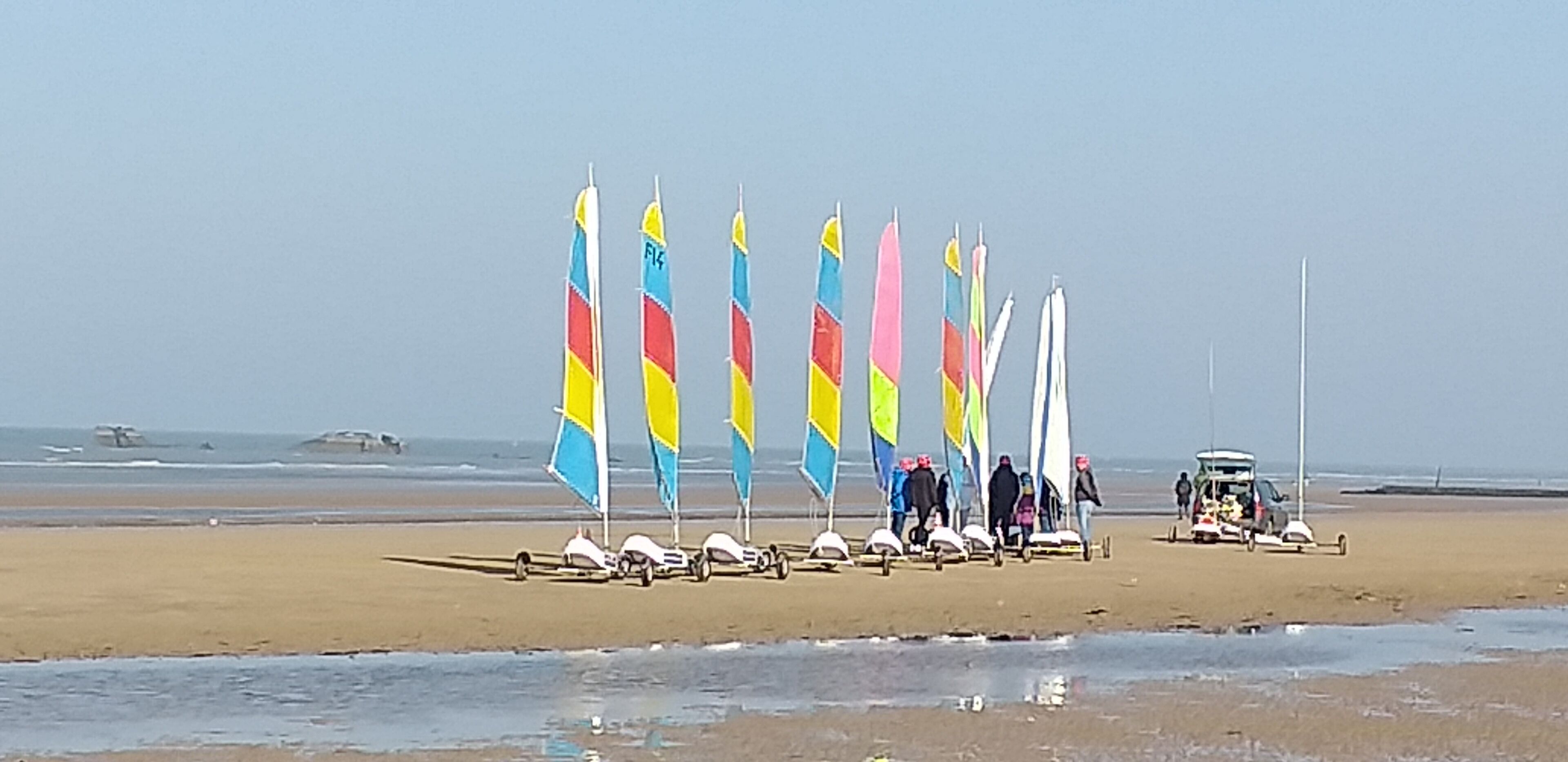 A beach with several sailboats and a vehicle parked on the sand.