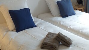 Ein Hotelzimmer mit zwei Betten, jeweils mit weißer Bettwäsche und blauen Kissen. Darüber an der Wand hängt ein gerahmtes Bild.