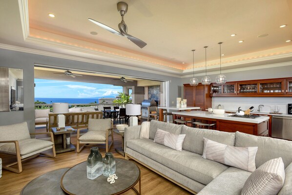 A spacious living area with a sofa, chairs, and a coffee table. There is a view of the ocean through large windows. - Sleeps 10, Family Favorite, Fully Upgraded Modern Renovation and Decorated (Kihei)