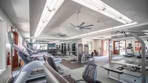 Een sportschool met loopbanden, krachttoestellen en een plafondventilator.