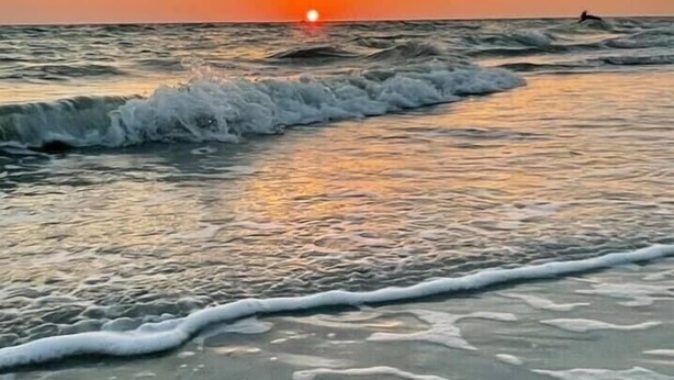 A beach scene with waves approaching the shore and a sunset in the background.